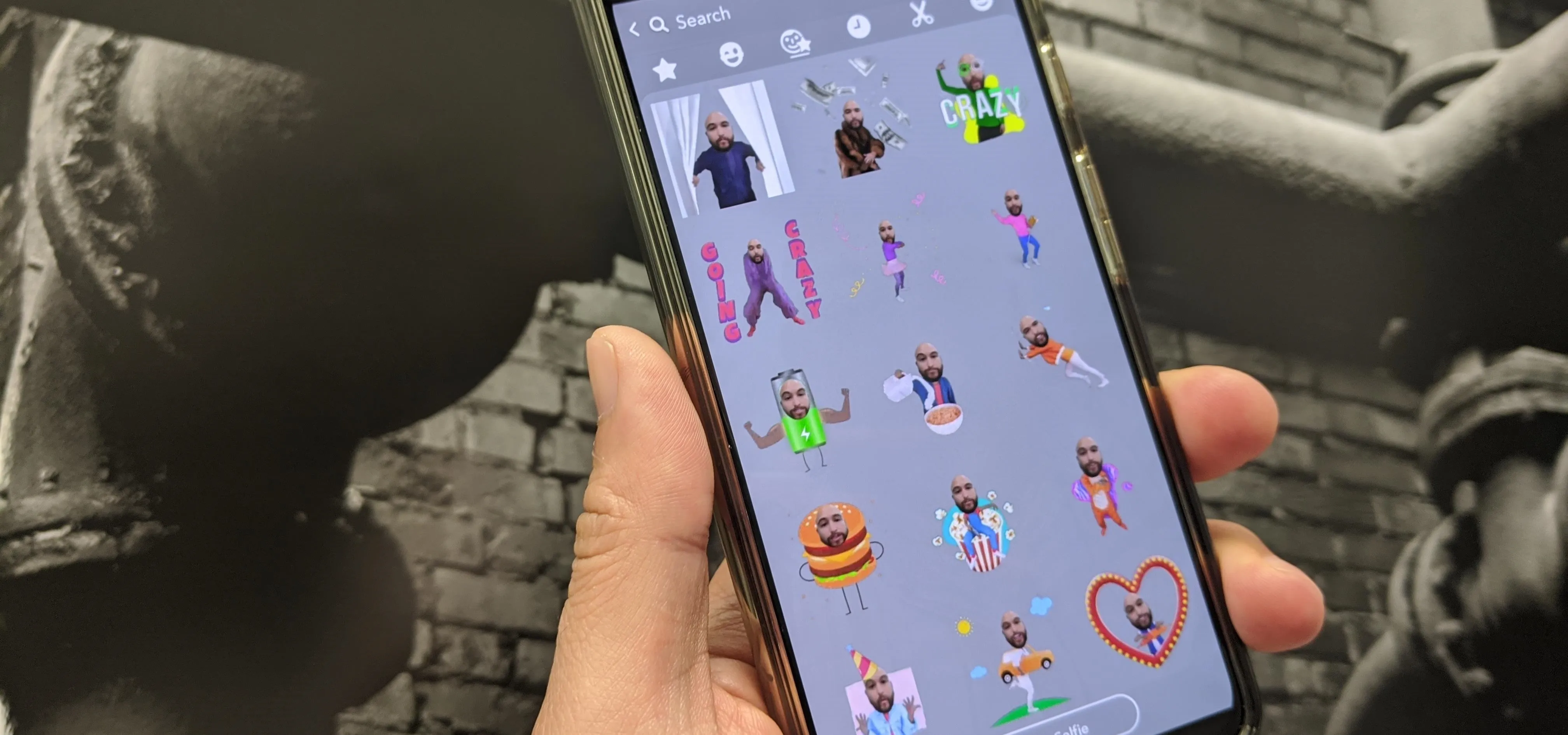 Hand holding a smartphone displaying a grid of colorful animated stickers.