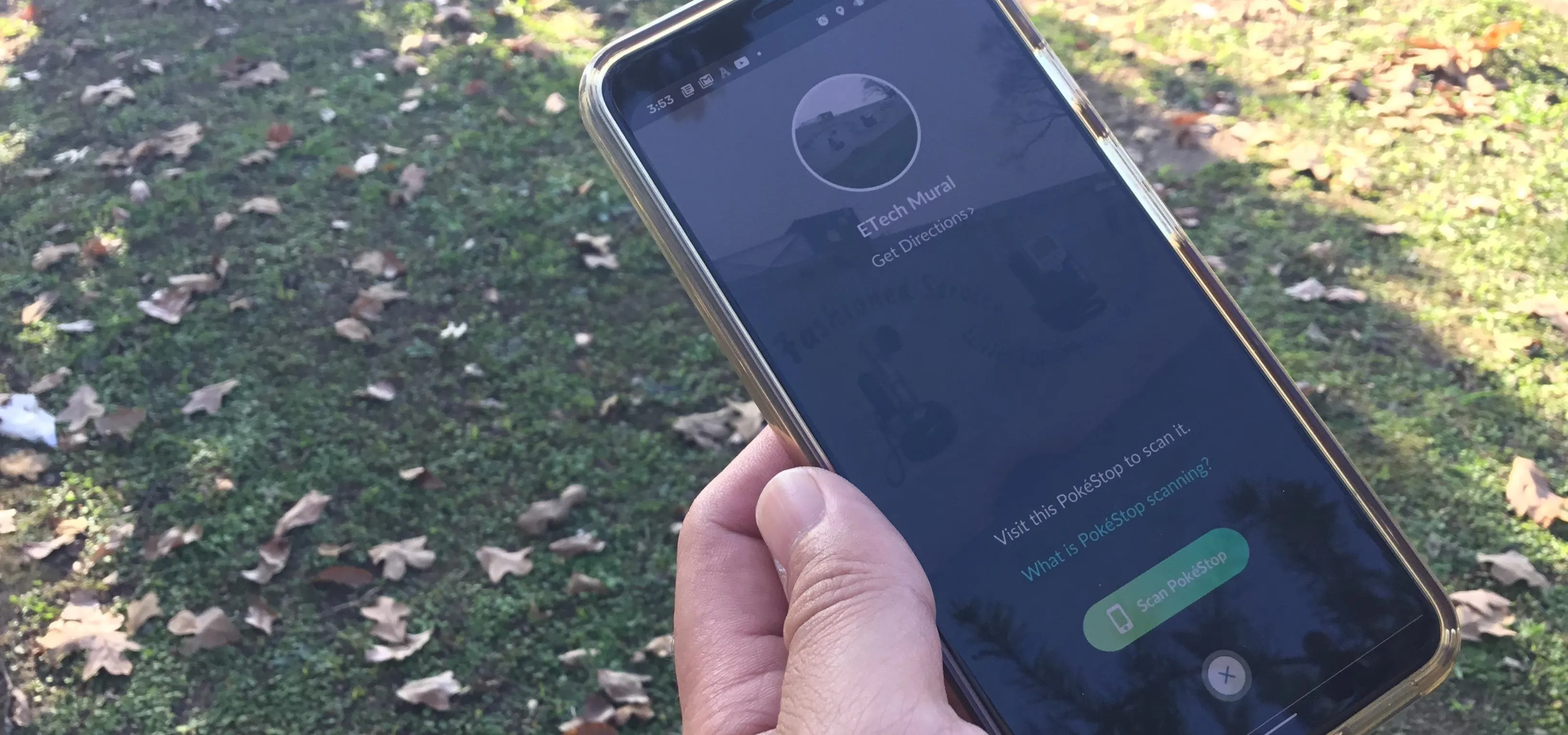 A hand holding a smartphone displaying a call interface outdoors on grass.