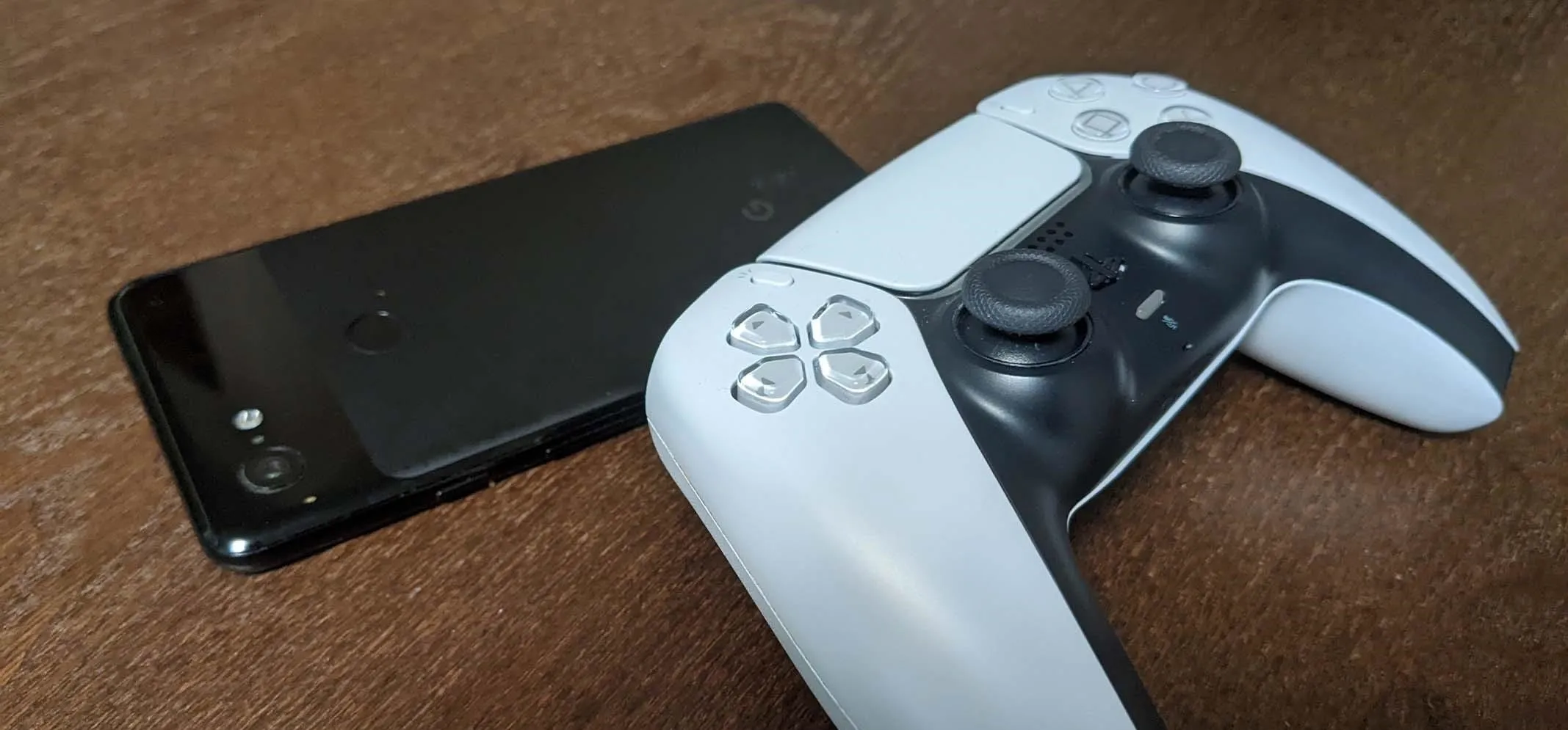 PlayStation 5 controller next to a smartphone on a wooden surface.