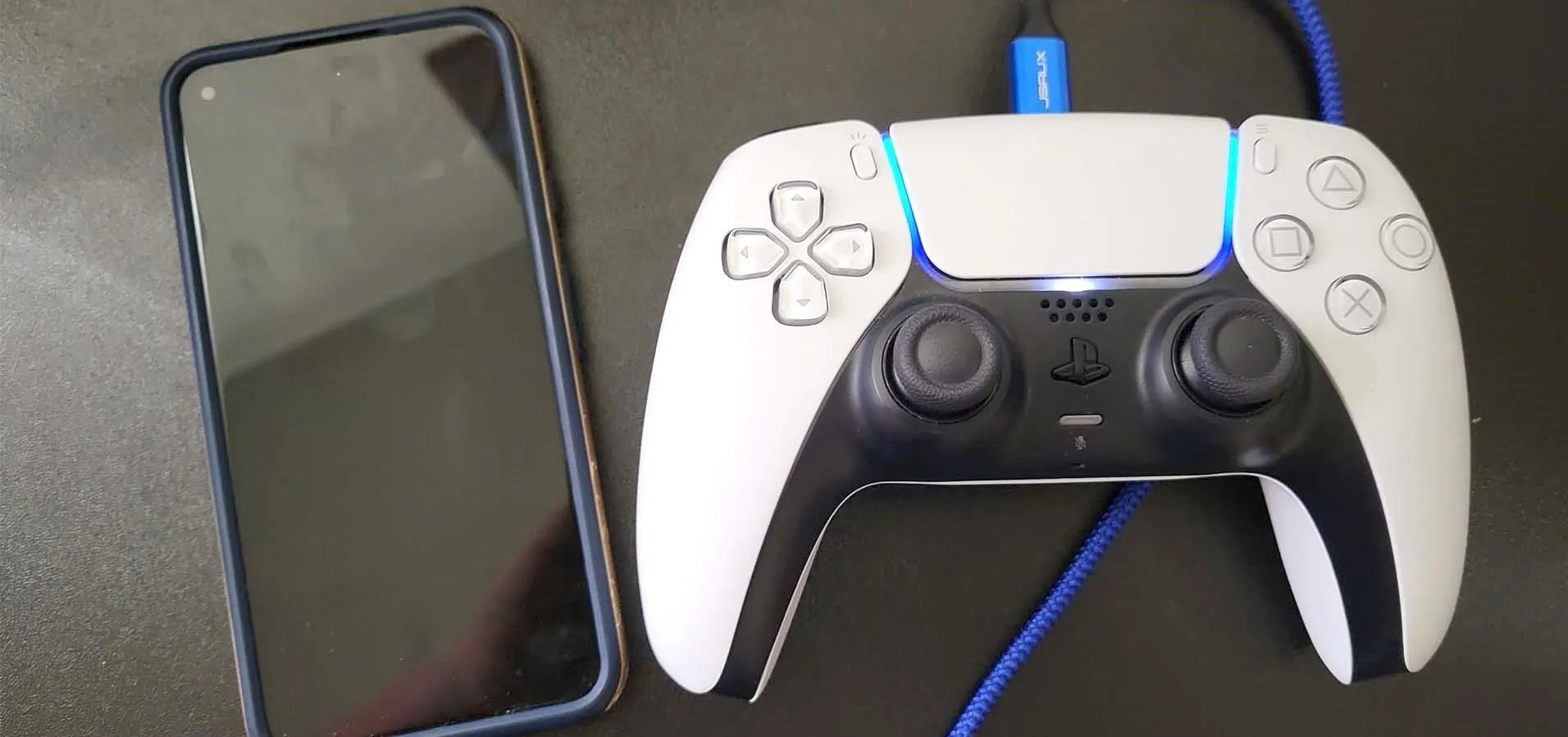 Gaming controller next to a smartphone on a dark surface.