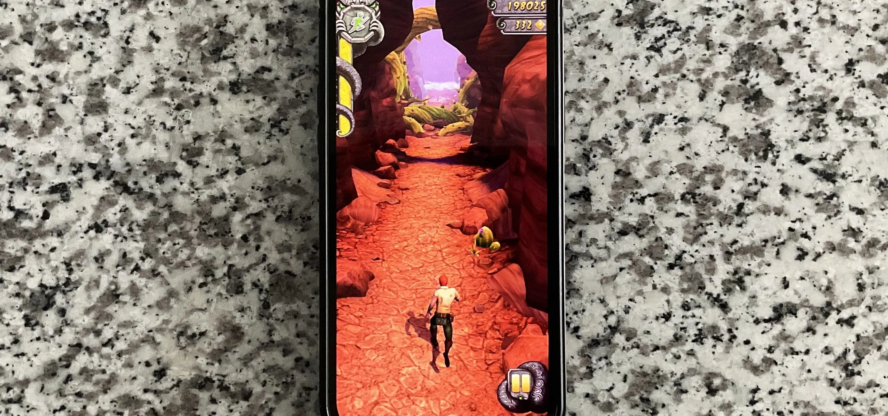 A mobile phone displaying a video game featuring a character running along a sandy path through canyons.