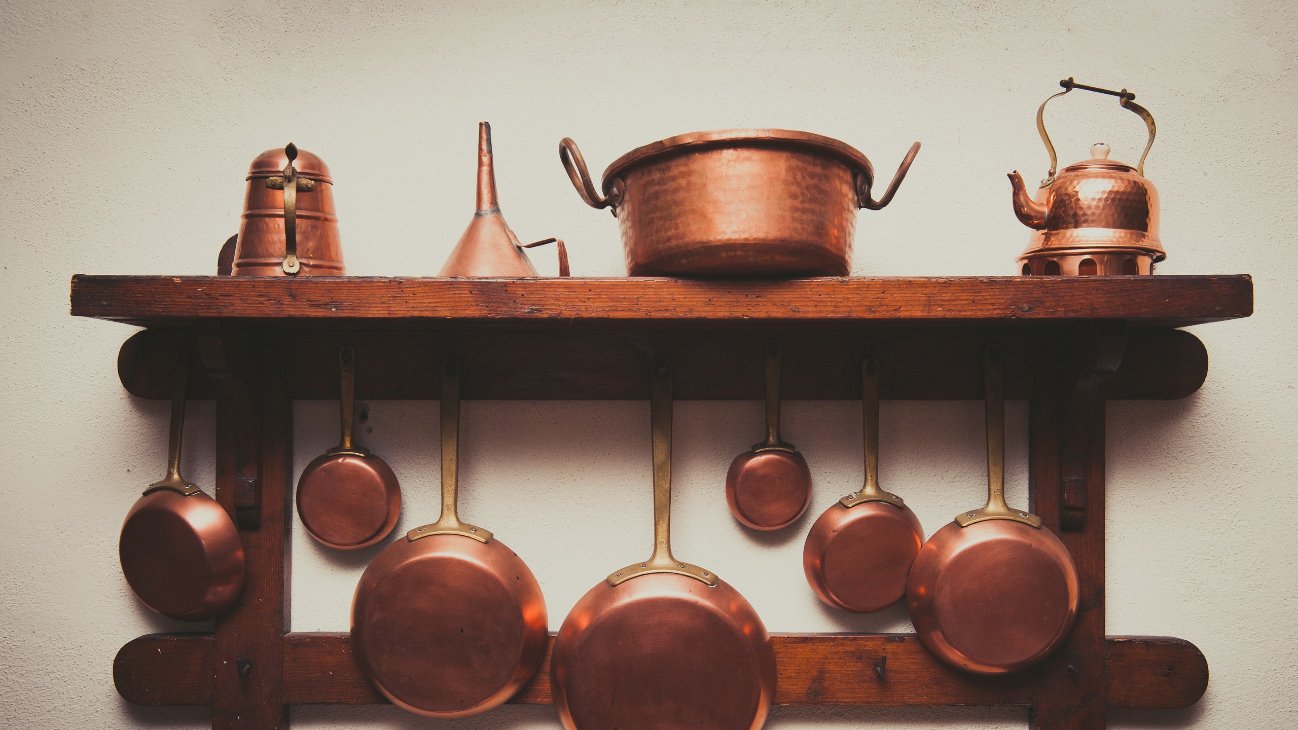 Photograph of copper cookware including a copper kettle and various pots and pans hanging off of and sitting on top of a...