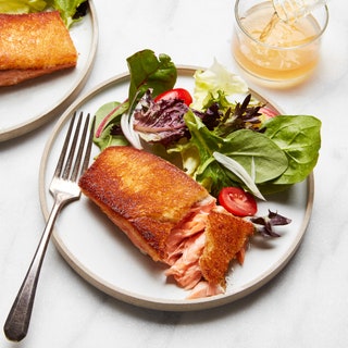 Two pieces of Brioche Crusted Salmon on plates served with salad and wine.