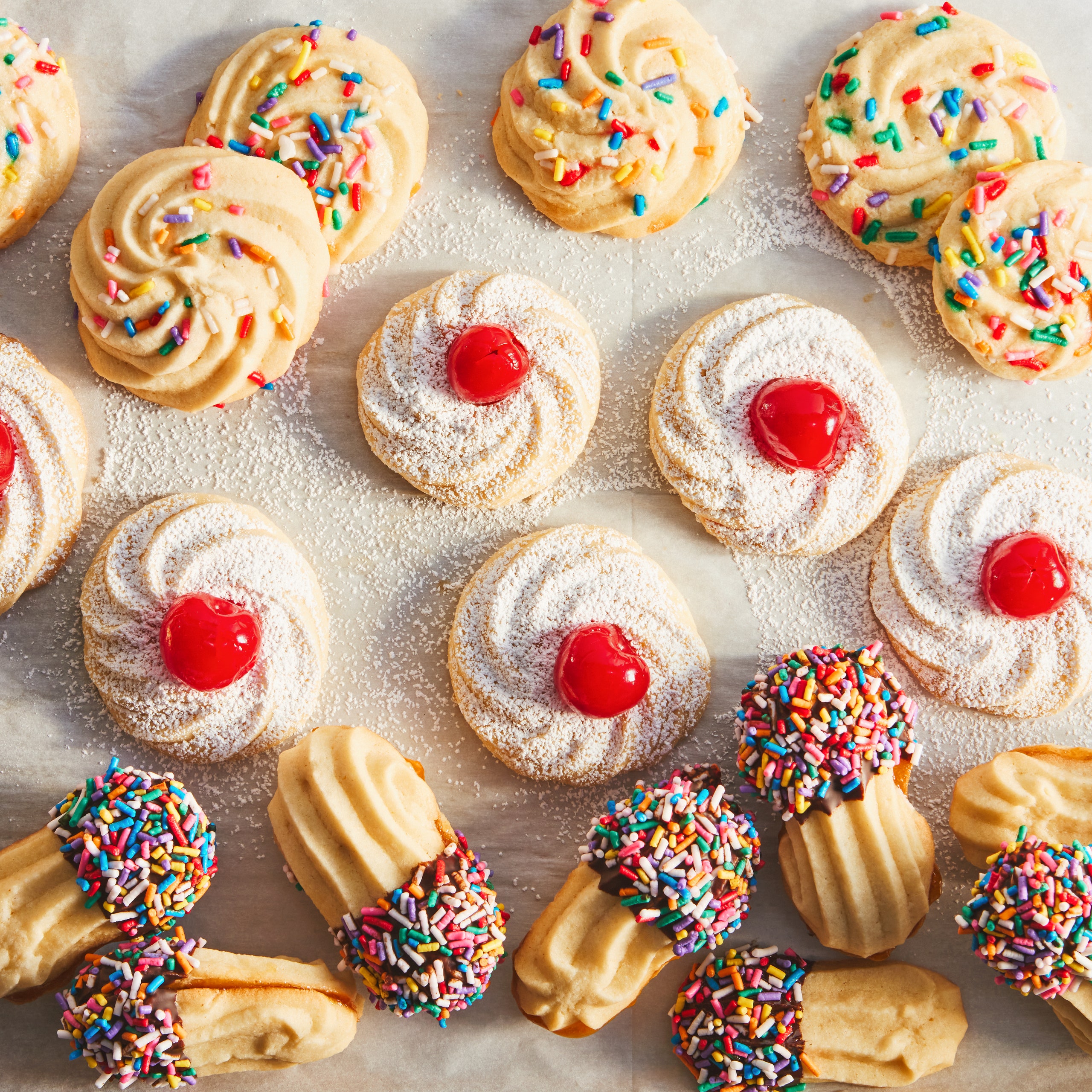 Sprinkle cookies maraschino cherry cookies and chocolatedipped sandwich cookies on a baking sheet.