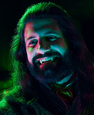 Kayvan Novak as Nandor the Relentless headshot with fangs, wearing a pink striped top.