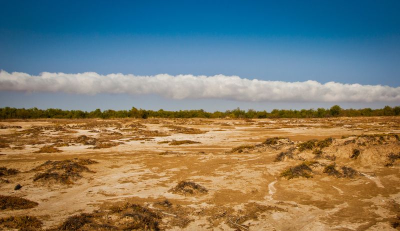 A large 'morning glory cloud' stretches across a blue sky over the Australian outback. 