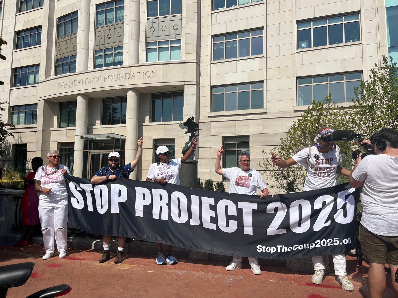 Protesters hold a Stop Project 2025 sign in front of the Heritage Foundation offices