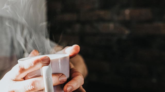 Hands gripping a hot, steaming mug of coffee 