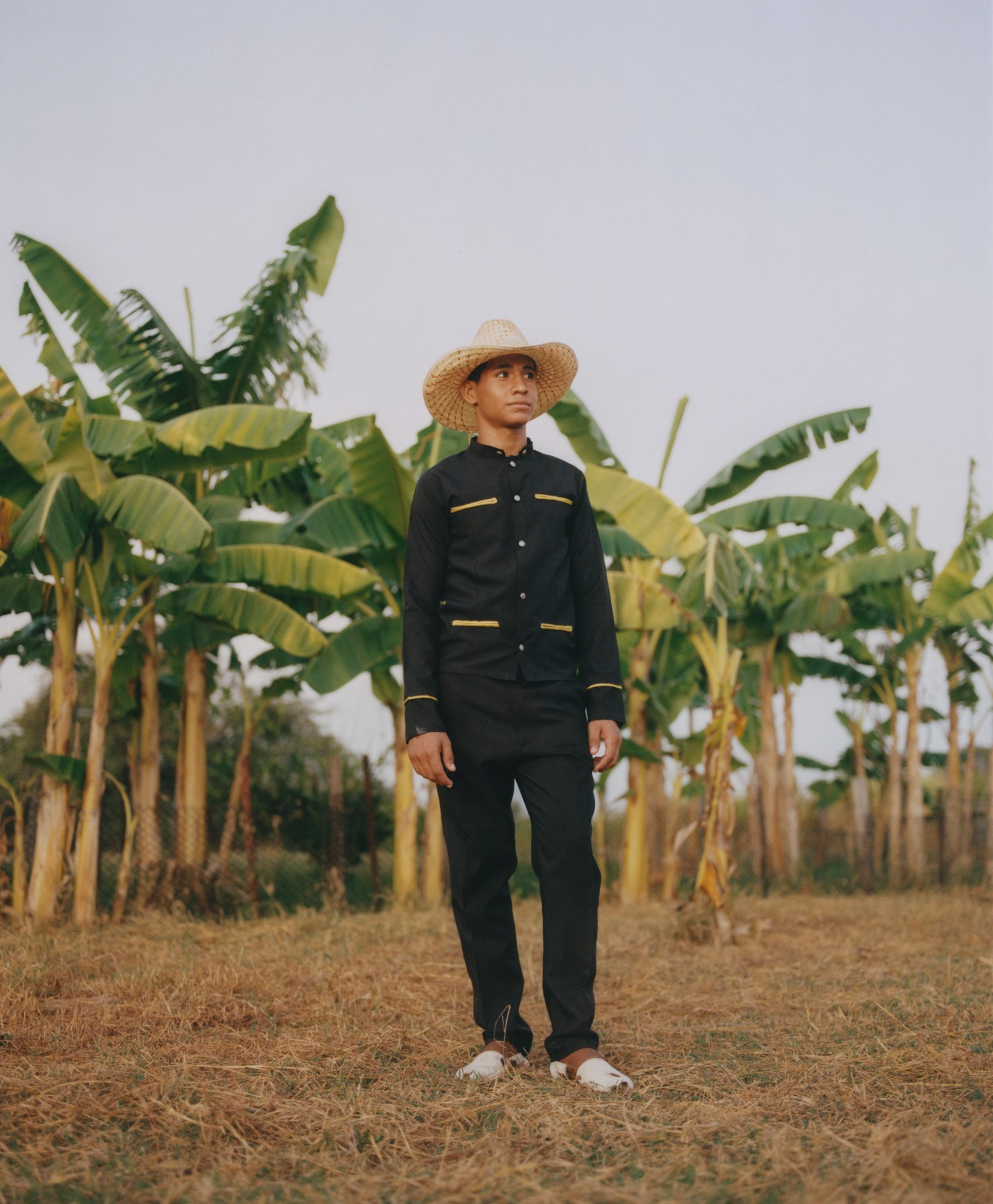 A young Venezuelan man stands in front of large green trees on the plains of Venezuela.