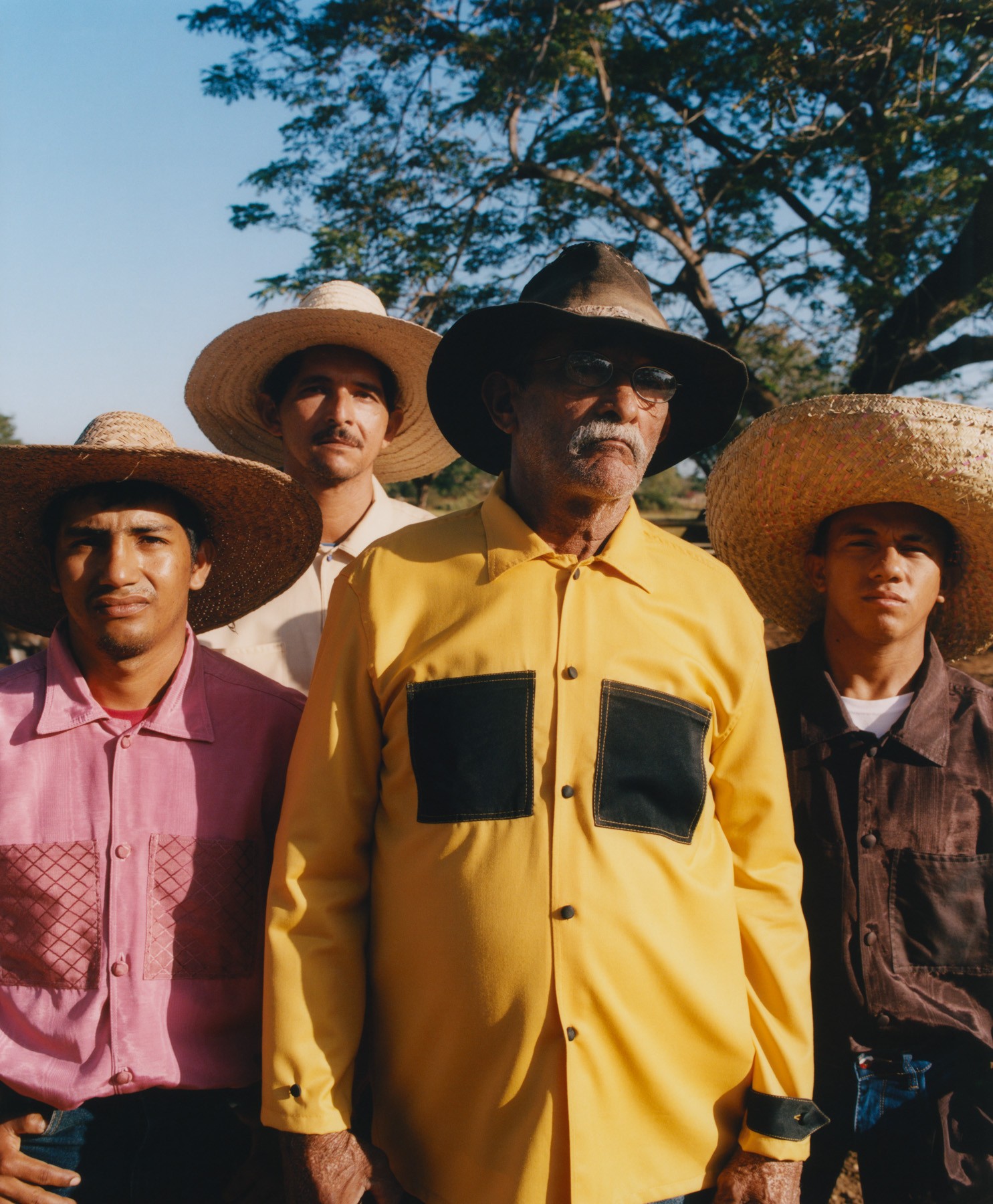 Four Venezuelan men wearing straw hats and collared shirts stand among each other, looking toward the camera.