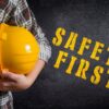 worker holding yellow hard hat with safety first text on chalkboard background