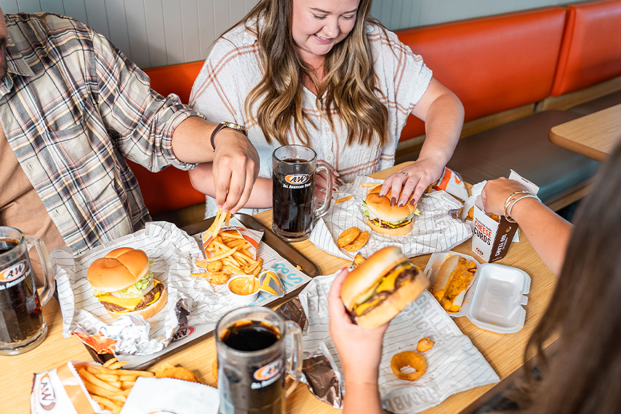 Group of people sitting at a table with A&W burgers, root beer, fries, and other menu items.