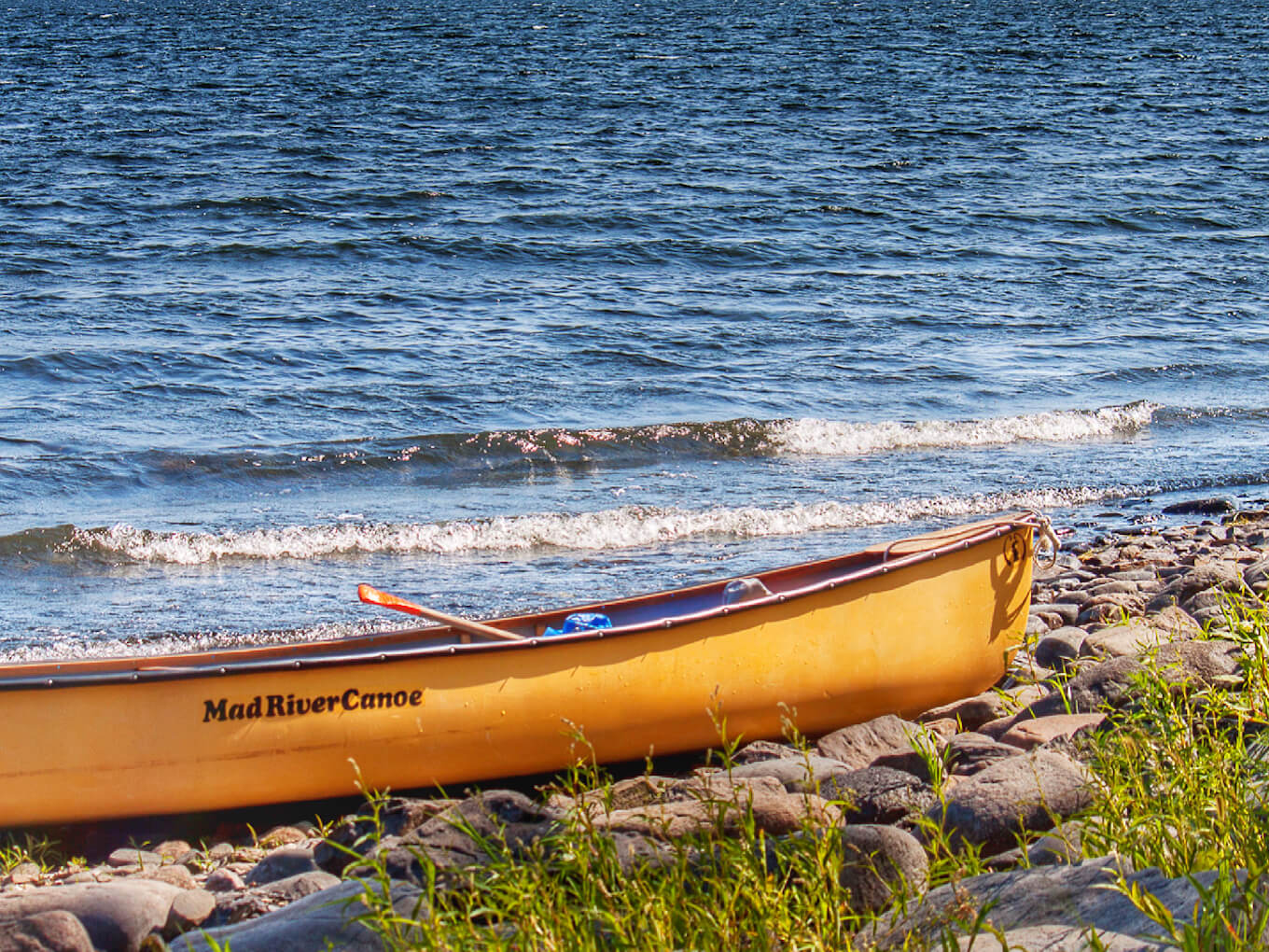 A yellow canoe on the shore of a blue lake demonstrates color contrast in photography.