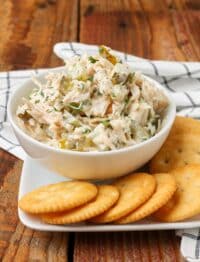 chicken salad with pickles in white bowl next to crackers on plate