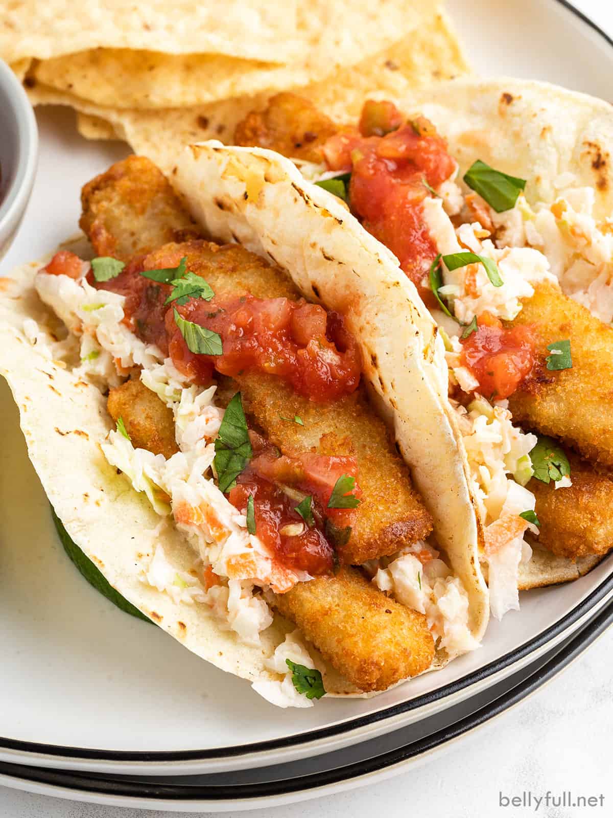 close up fish stick tacos with coleslaw and salsa on plate