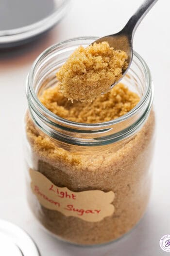 A spoon of brown sugar above a jar of brown sugar