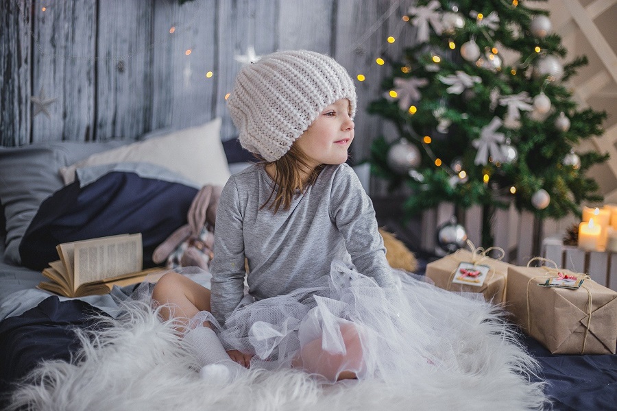 Elf on The Shelf Names Little Girl Sitting on a Bed with a Christmas Tree in the Background