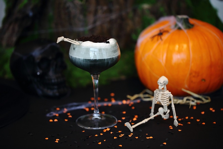 50+ Halloween Margarita Drinks & Halloween Cocktail Recipes Close Up of a Cocktail with a Small Skeleton Next to it and a Pumpkin in the Background