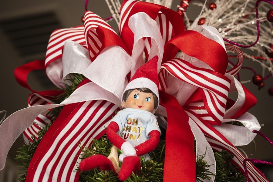 Easy Elf on The Shelf Ideas an Elf Against a Big Christmas Ribbon That's Red and White