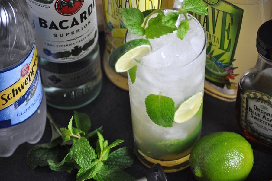 Easy Low Cal Mojito Recipe Close Up of a Mojito Garnished with Lime Slices and Mint Sprigs Next to Bottles of Alcohol