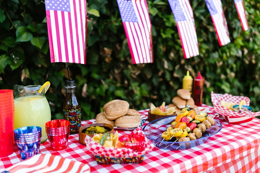 Easy 4th of July Recipes a Food Table with Hamburgers, Hot Dogs and Condiments at a Patriotic Party with American Flag Bunting