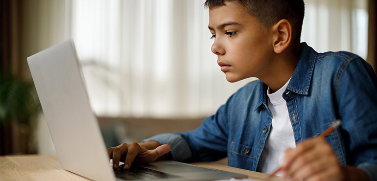 A young boy sits at a desk with his laptop. 