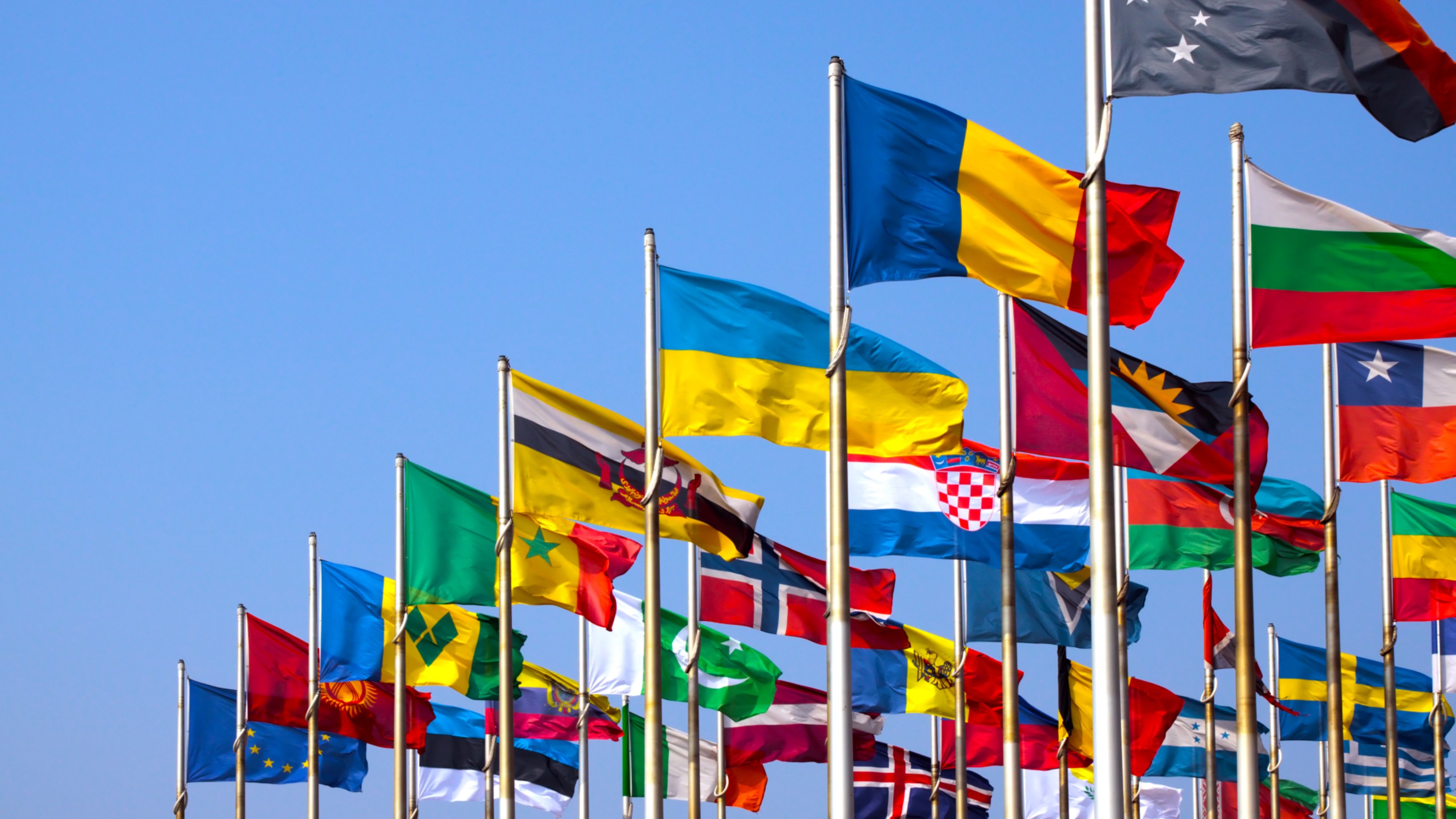 Multiple country flags on poles against a clear blue sky, representing international diversity and unity.