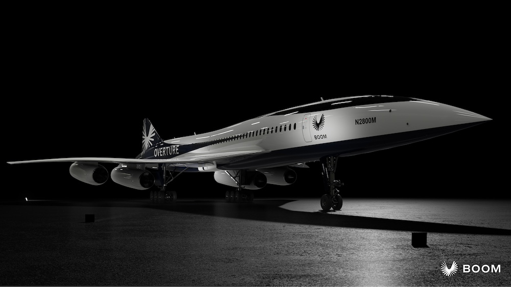 A sleek, black and white Boom supersonic jet, labeled "Overture", on display in a dimly lit hangar.