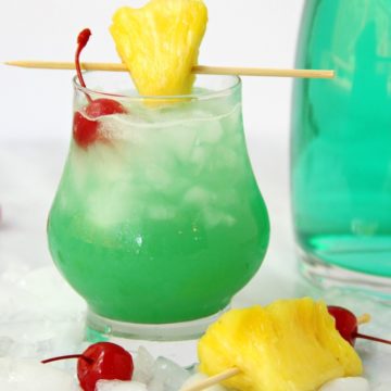 A green cocktail garnished with pineapple and a cherry.