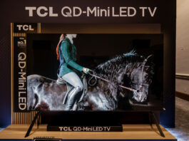 TCL 115QM7K TV on a stand at a CES 2025 showcase.