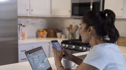 A woman using her smartphone and laptop in the kitchen.