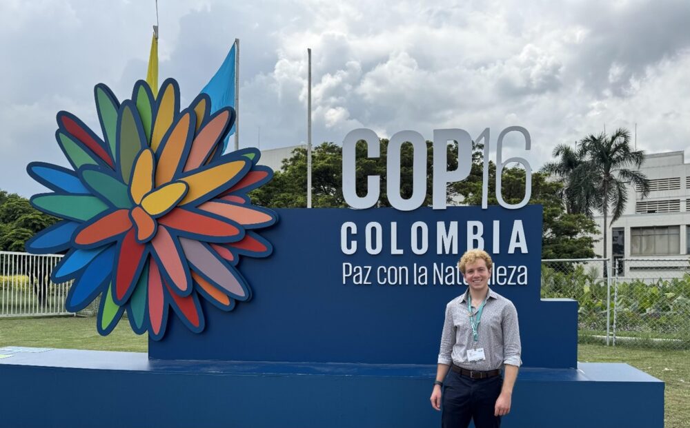 A person stands in front of a large sign that reads, "COP16 Colombia Paz con la naturaleza".