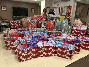 Two staff members pose behind rows and rows of colorfully wrapped presents