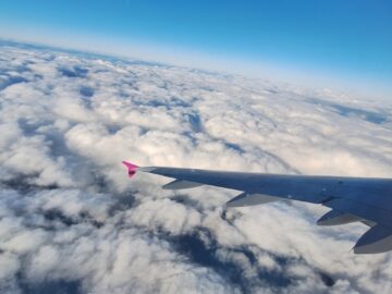 pink wingtip against a partly cloudy sky and horizon while flying