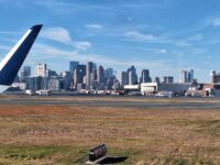 a plane wing on a runway with a city in the background