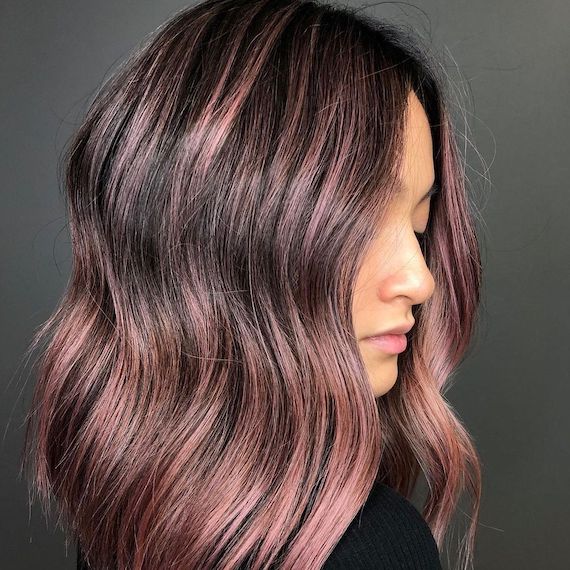 Model looks to the side showing her dark brown hair featuring dusky pink highlights. 