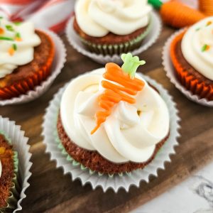 A close-up of one of several carrot cake cupcakes with cream cheese frosting and carrot decorations