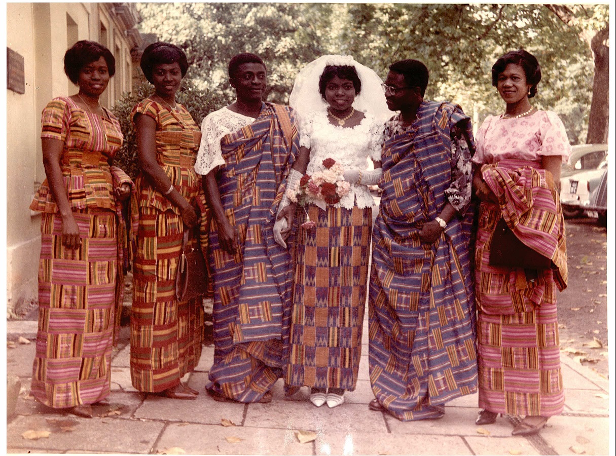 A bride, groom, and their wedding party, dressed in a mixture of white lace and ?kente cloth, c. 1960s