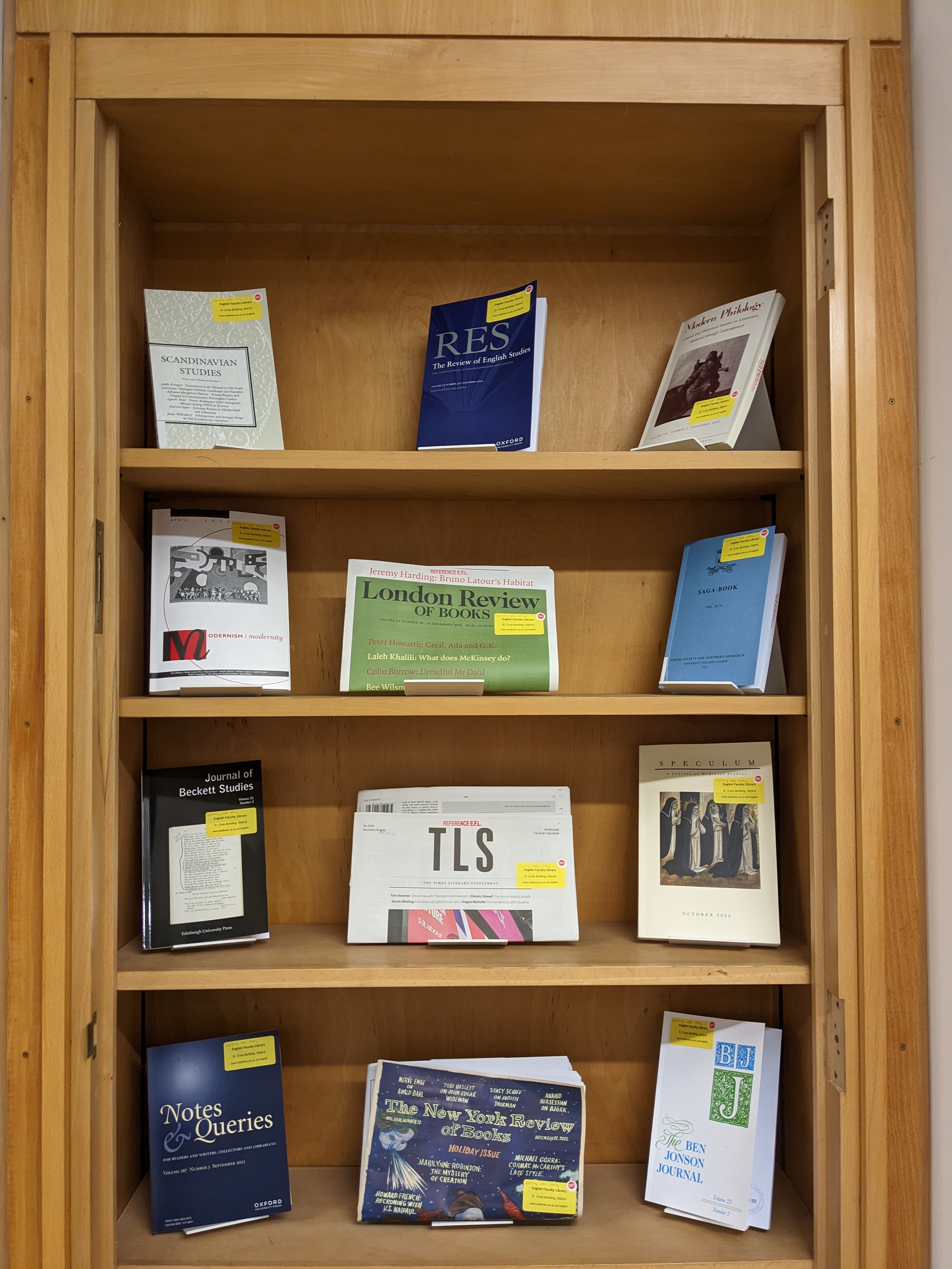 Wooden shelf with 9 journals and three newspapers displayed on it