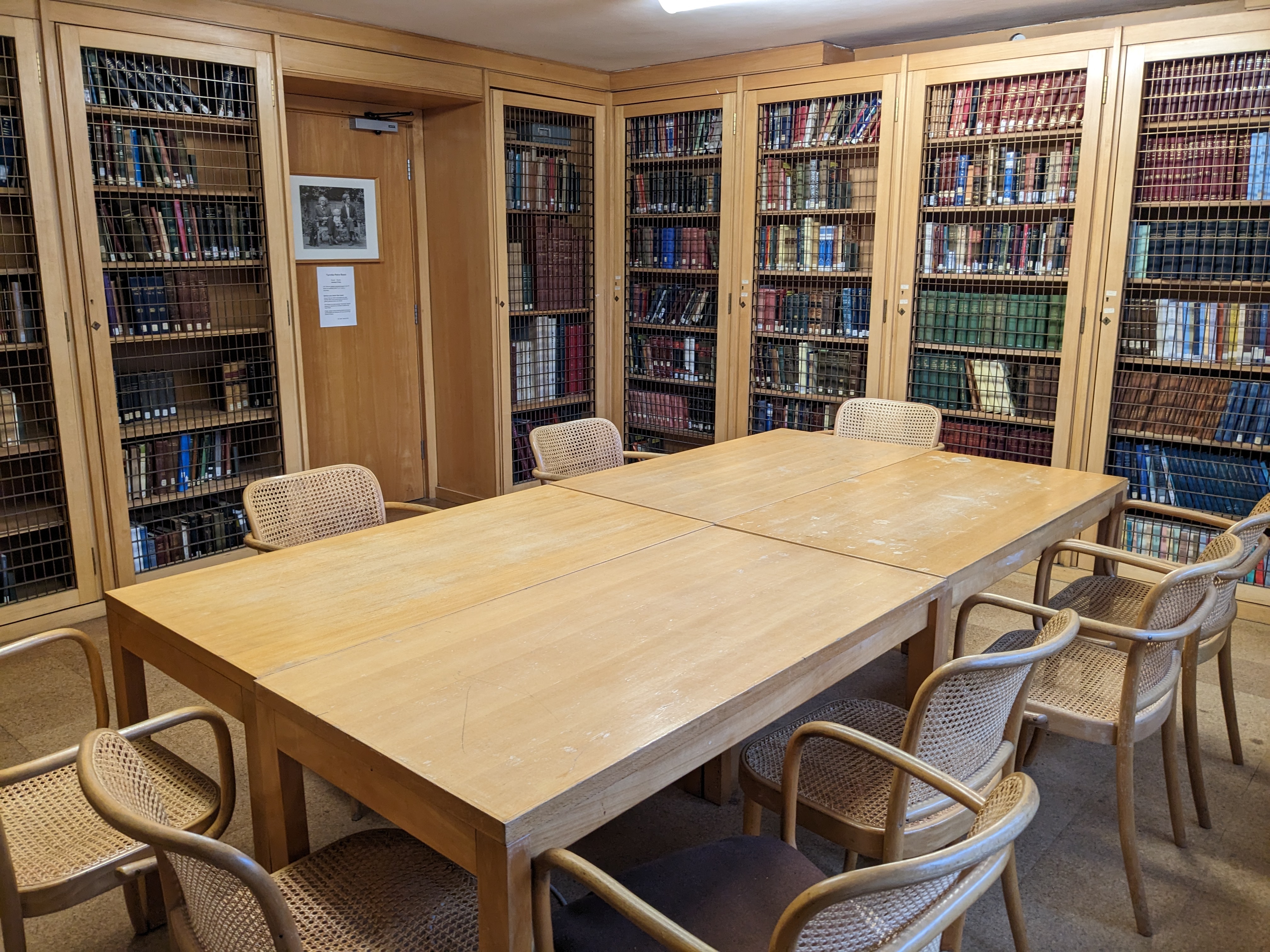 A long desk with 9 chairs around it, and books in cages around the sides of the room