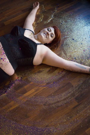 A fat woman creates a snow angel out of glitter on a wood floor