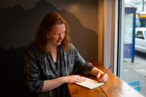 A woman with red hair wearing a blue blouse takes notes