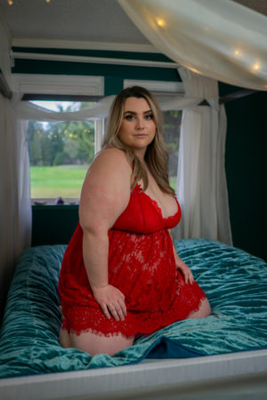 A fat woman in red lingerie looking confidently at the camera during a photo session in the PNW