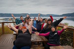 A group of fat friends pose playfully around a table on a lake in the PNW