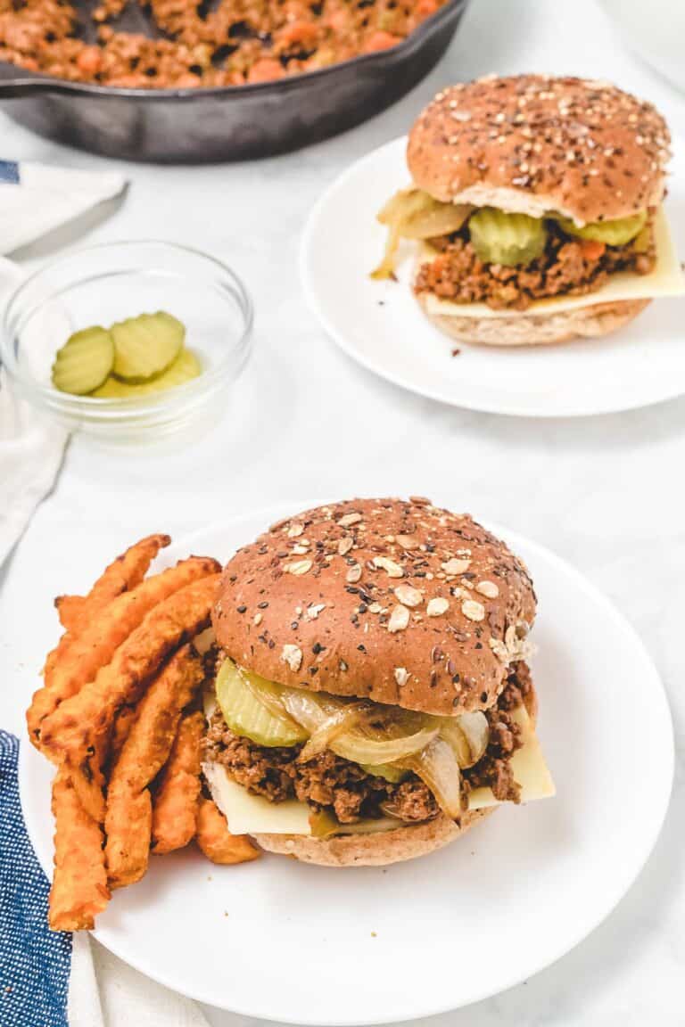 two white plates with healthy sloppy joes over whole wheat buns and sweet potato fries to the side.