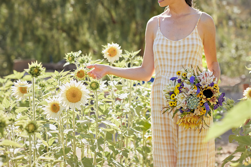 Woman in a yellow and white checked jumpsuit admires sunflowers