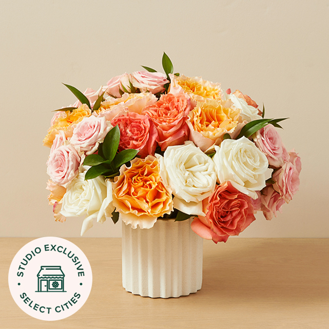 Bright bouquet of yellows, oranges and pinks in a dark vase.