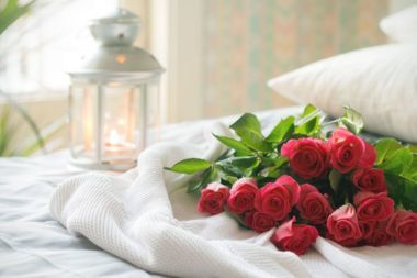 Red roses laid out on a white bed with a lantern in the background.