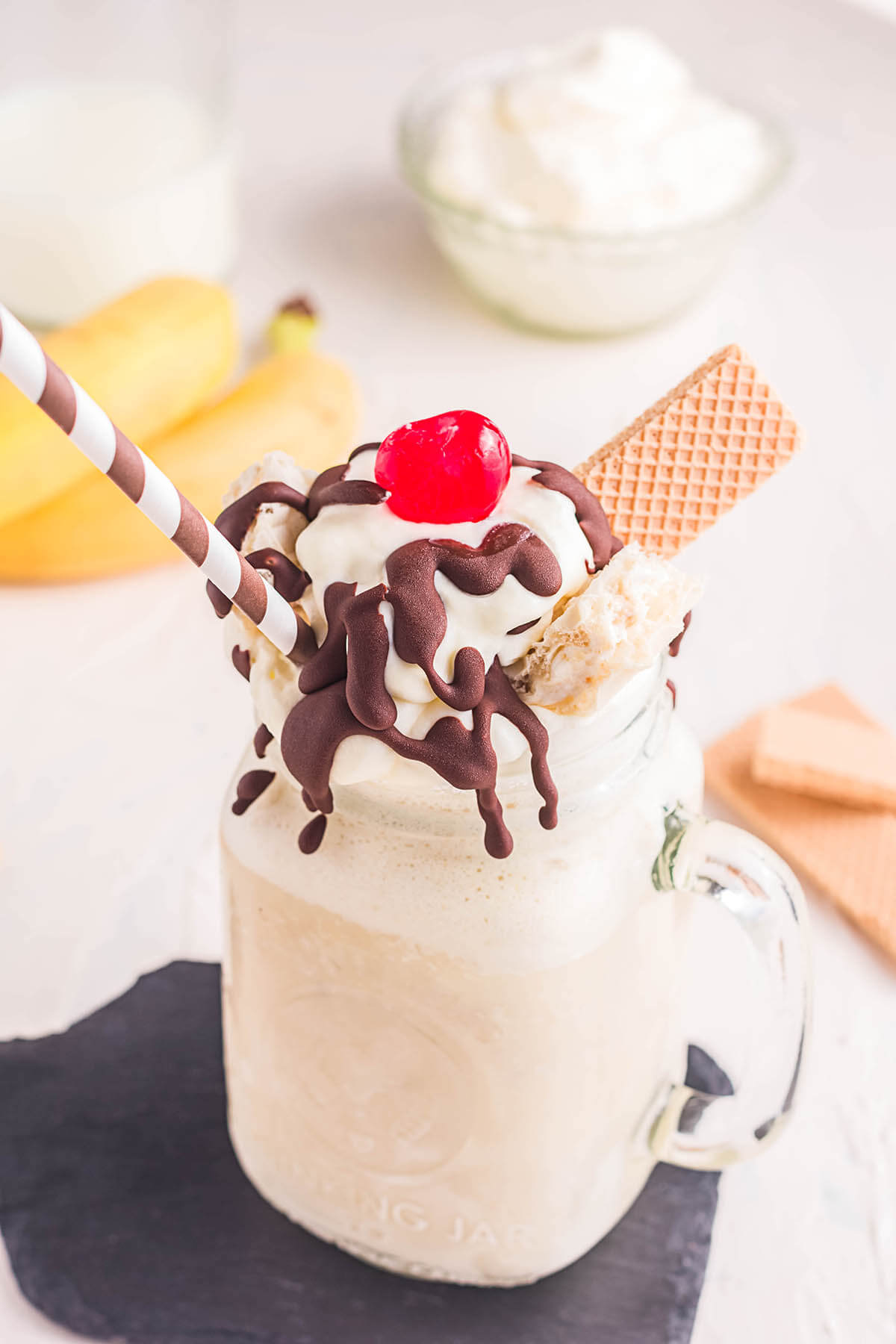 Mug filled with a malt topped with whipped cream, drizzled chocolate, vanilla wafer and topped with a cherry.