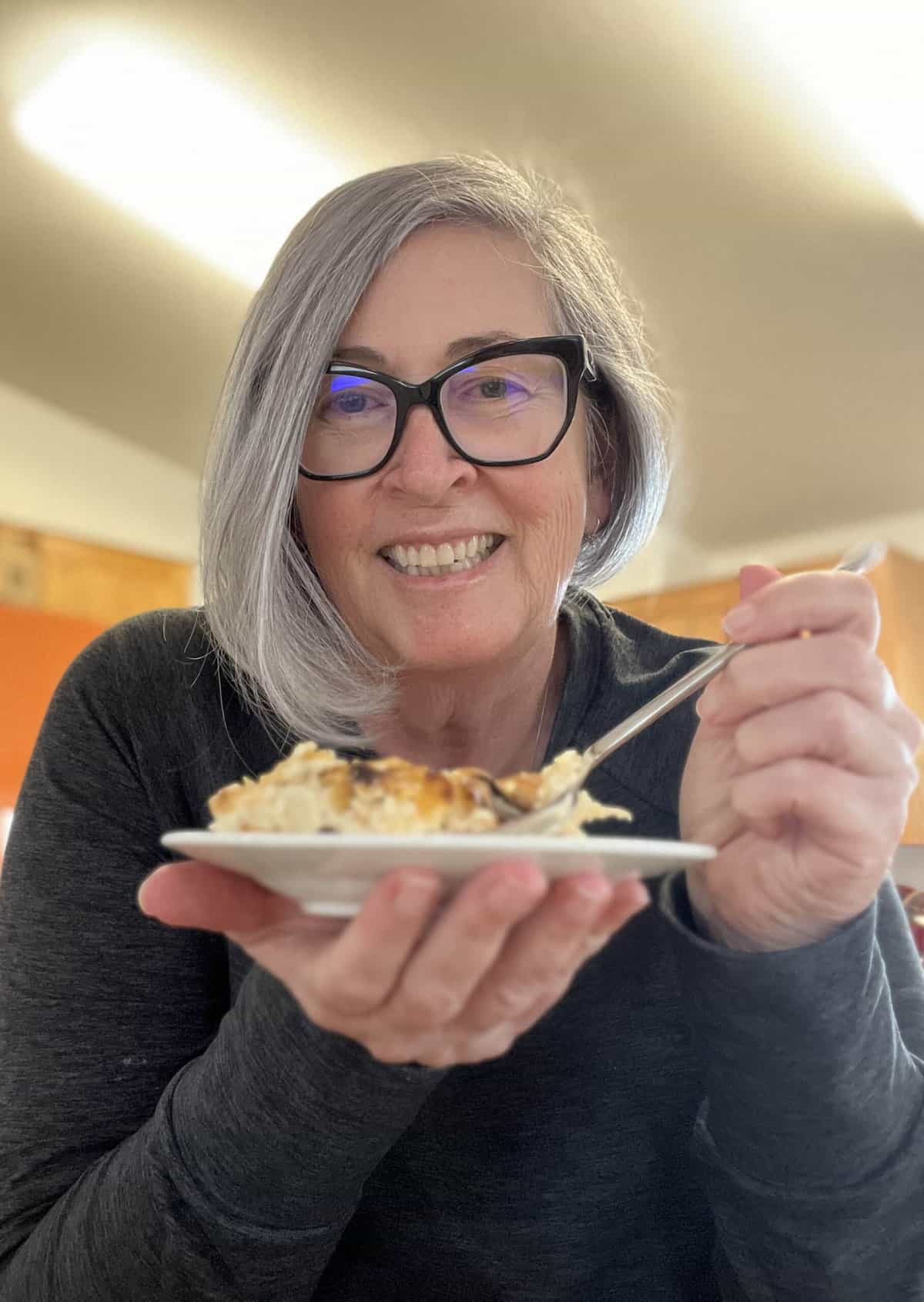 Blogger Deb Clark smiling at camera holding a plate filled with a casserole.